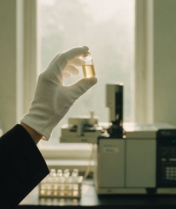 Un flacon d'échantillon tenu à la lumière devant un chromatographe en phase gazeuse.