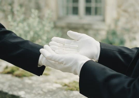 Deux mains gantées s'avancent, paumes ouvertes, offertes.
